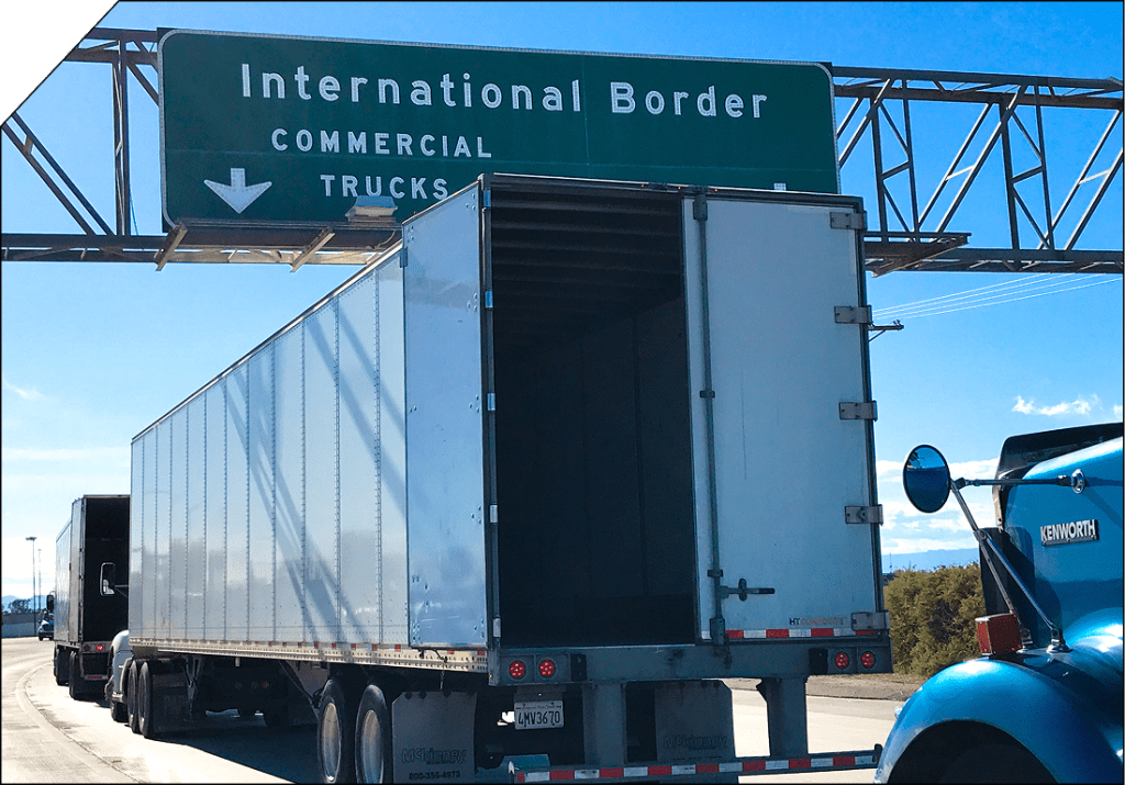 Heavy-duty freight truck travelling on a highway beneath an international border sign, representing cross-border less-than-truckload shipping.